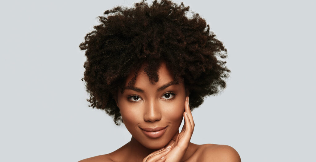 Enjoying her beauty. Attractive young African woman looking at camera and smiling while standing against grey background